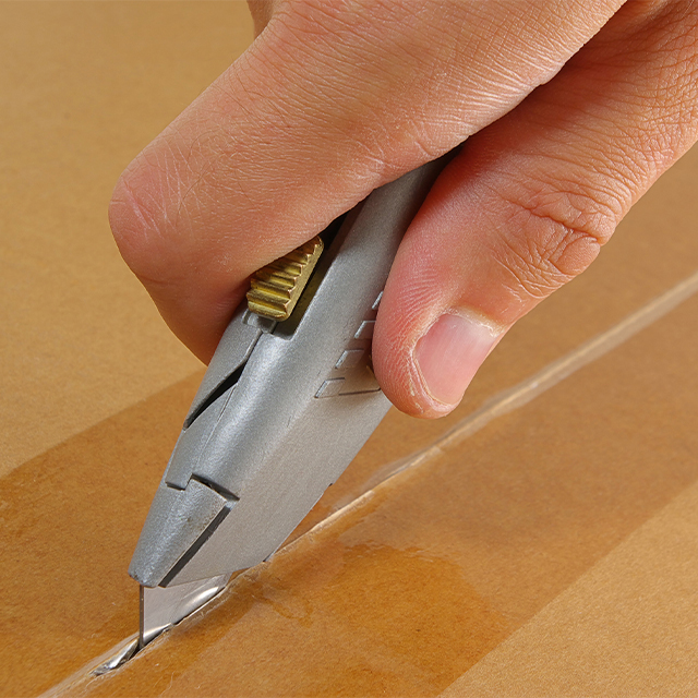 Picture of a stanley knife cutting into a box