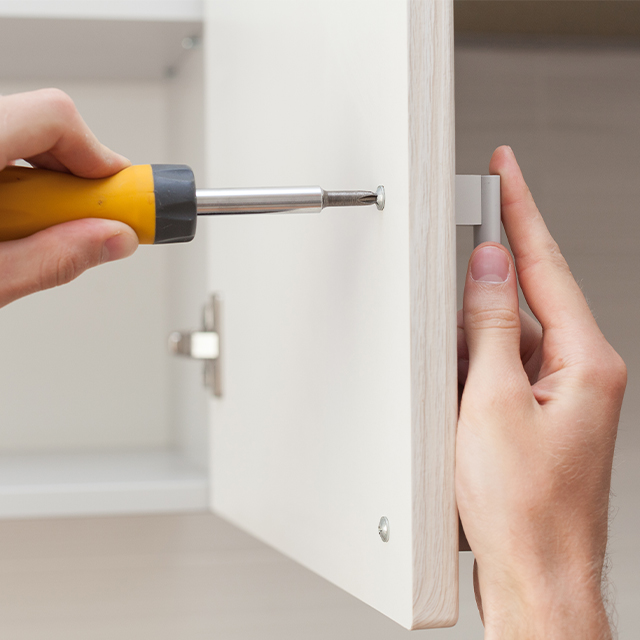 Picture of a screwdriver screwing  a screw into a cupboard door
